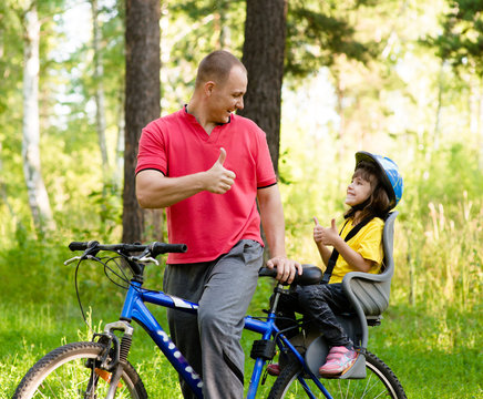 happy father and his cute daughter outdoors in forest on a bike