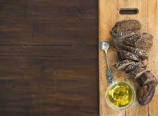 Dark baguette cut in slices with olive oil on a rustic wooden bo