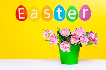Pink flowers in green pot on table, word Easter