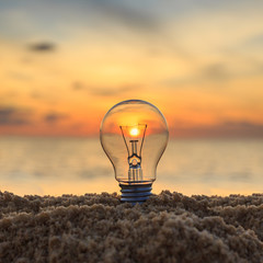 Close up light bulb on sunset beach, energy concept