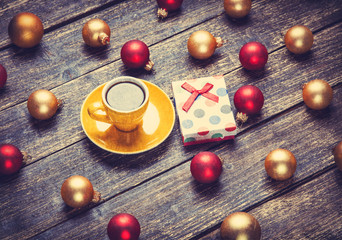 Cup of coffee and christmas balls and gift on wooden table.