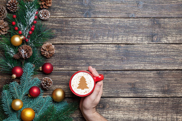 Cappuccino with christmas tree shape and male hand on wooden tab