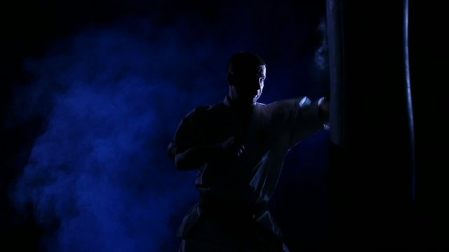 Silhouette karate man practicing on the sandbag on blue