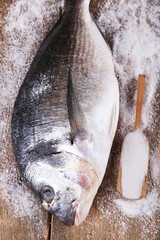 Fresh fish and salt in spoon on wooden background