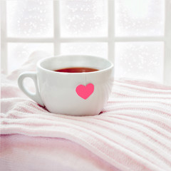 Hot tea on knitted sweater and heart teabag, snowfall outside