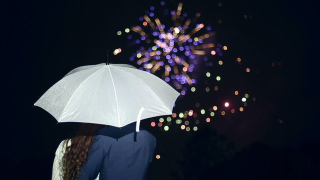 People stand under an umbrella and watch fireworks.