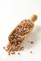 Wooden scoop with buckwheat grain on white background