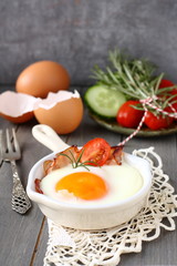Fried egg with bacon in ceramic pan on wooden background
