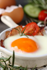 Fried egg with bacon in ceramic pan on wooden background