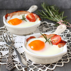 Fried egg with bacon in ceramic pan on wooden background
