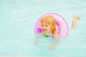 Happy baby girl with swim ring swimming in pool