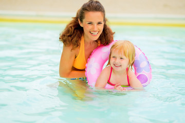 Fototapeta na wymiar Portrait of happy mother and baby girl with swim ring swimming