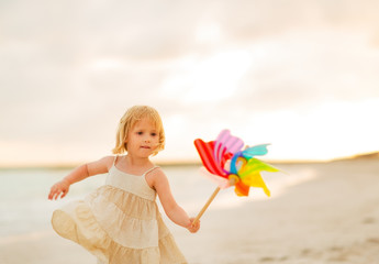 Baby girl playing with colorful windmill toy on beach