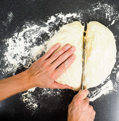 Hands cutting a lump of dough into two pieces