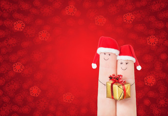 Fingers faces in Santa hats with gift box. Happy couple celebrat