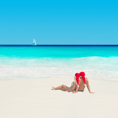Fototapeta na wymiar couple in christmas hats at ocean beach with yacht, new years va