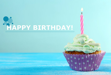 Delicious birthday cupcake on table on light blue background