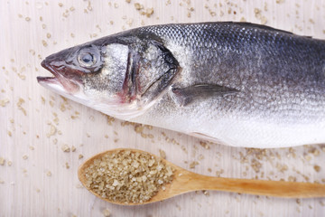 Fresh fish and salt in spoon on wooden background