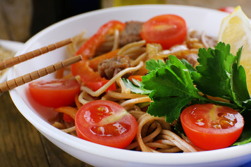 Chinese noodles with vegetables and roasted meat in bowl