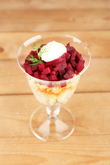 Russian herring salad in glass bowl on wooden table background