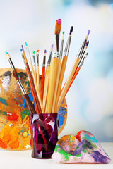 Paint brushes with paints and palette on bright background