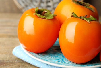 Ripe persimmons on plate, on wooden background