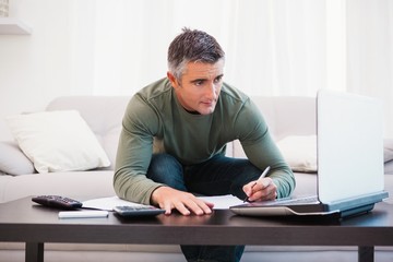 Concentrated man using laptop and taking notes