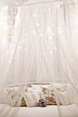 White cozy bed with vintage pillow and christmas lights