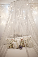 White cozy bed with vintage pillow and christmas lights
