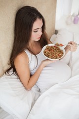 Obraz na płótnie Canvas Pregnant brunette eating cereal in bed