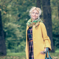 trendy Beautiful senior woman in a yellow coat walks in the park