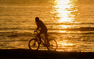 Naklejka na ściany i meble Girl riding bicycle by sea against sunset