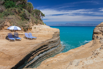 Beach sunbeds and umbrella on a cliff above the blue sea