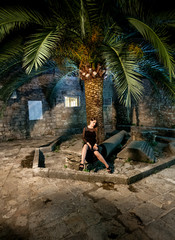 young woman in black cocktail dress sitting on old street at nig