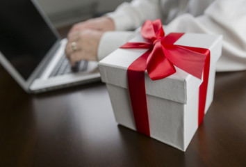 White Gift Box with Red Bow Near Man using Laptop