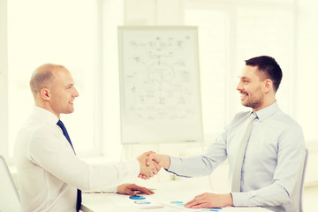 two smiling businessmen shaking hands in office