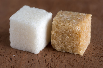 cubes of brown and white sugar on  board of mahogany