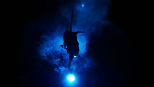 Aerial acrobat woman on circus stage. Silhouette on a blue