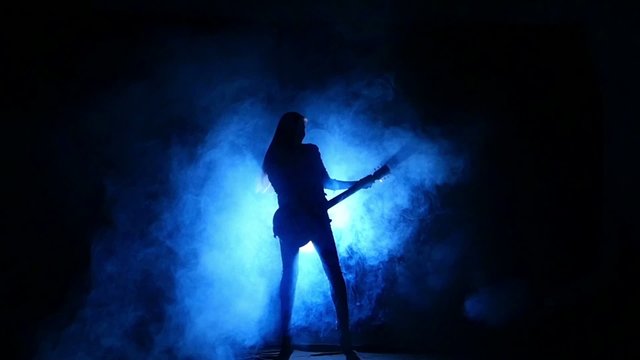 Silhouette of a young girl playing on electric guitar. Slow