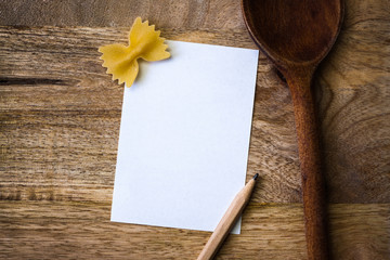 Note for recipe on wooden cutting board with kitchen spoon