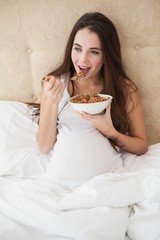 Pregnant brunette eating cereal in bed