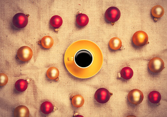 Hot coffee and christmas balls on jute background.
