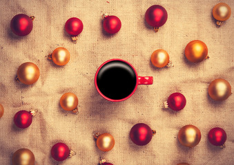 Hot coffee and christmas balls on jute background.
