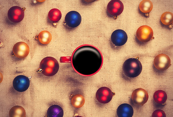 Hot coffee and christmas balls on jute background.