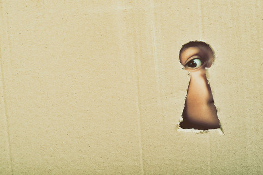 Eye looking through a conceptual keyhole on cardboard, close up