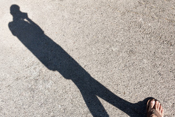 Shadow of someone wearing shoes standing on the road