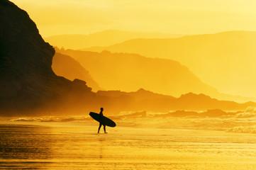 Surfer, der bei nebligem Sonnenuntergang ins Wasser eindringt