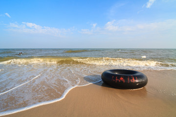 Fototapeta na wymiar Black life ring for swimming on beach with wave