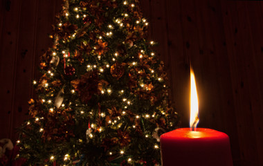 Christmas candle glowing brightly with a decorated Christmas tree lighted behind