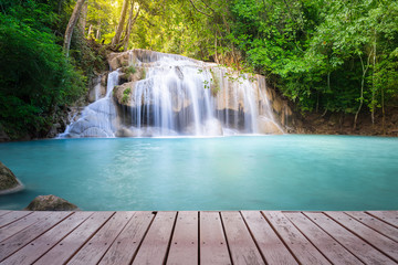 Waterfall, green forest in Erawan National Park in Thailand montage with wooden floor. Landscape with water flow, tree, river, stream and rock at outdoor. Beautiful scenery of nature for vacation.
